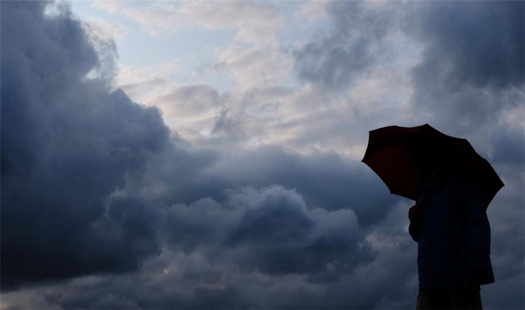 Ein Mann geht mit einem Regenschirm vor aufziehenden dunklen Wolken spazieren. (Symbolbild)