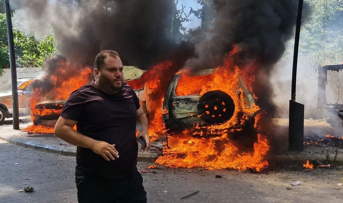 Ein Mann läuft vor brennenden Autos, die bei einem israelischen Luftangriff in der libanesischen Hafenstadt Sidon in Brand geraten sind.