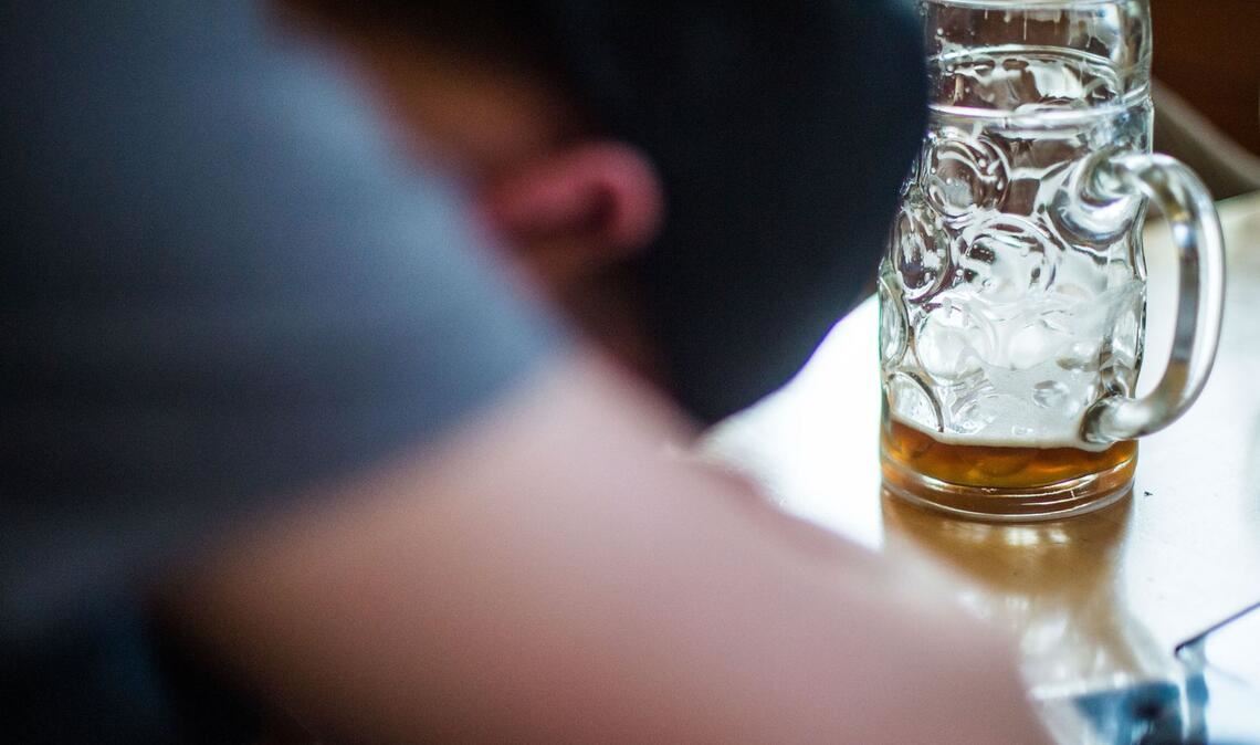 Ein Mann schläft in einer Gastwirtschaft vor einem fast leeren Maßkrug. Wer an den Karnevalstagen ein paar Gläser mehr trinkt, könnte einen ungebetenen Gast bemerken: den Kater nach dem Rausch.