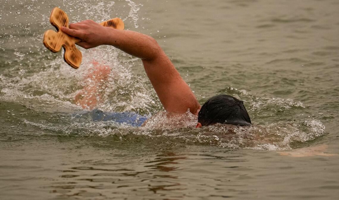 Ein Mann schwimmt mit einem von drei Holzkreuzen, die der orthodoxe Erzbischof Teodosie bei Harsova in die Donau geworfen hat, damit die Menschen sie zurückholen können, während eines Gottesdienstes einen Tag vor dem Dreikönigsfest.