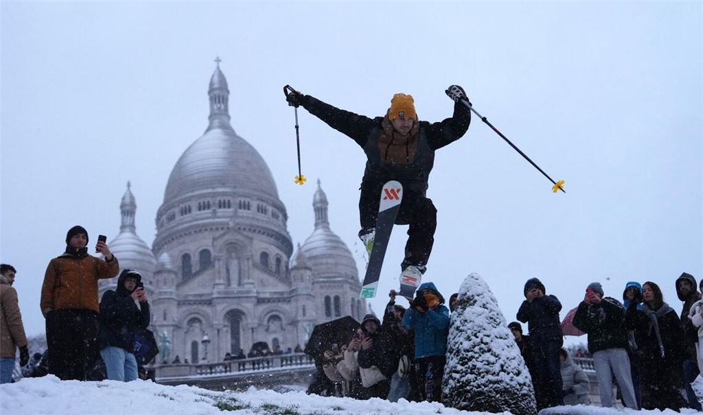 Ein Mann springt mit seinen Skiern den Hügel bei der Basilika Sacre-Coeur hinunter, während es im Viertel Montmartre schneit.