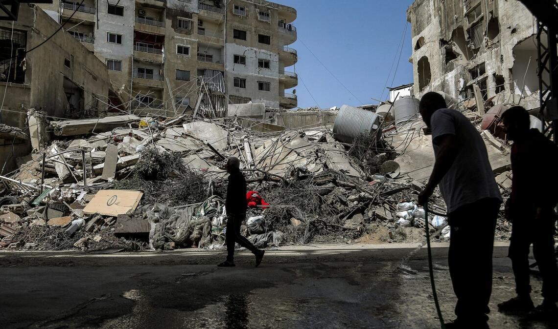 Ein Mann spritzt nach israelischen Luftangriffen im Libanon Wasser auf eine Straße vor zerstörten Gebäuden.