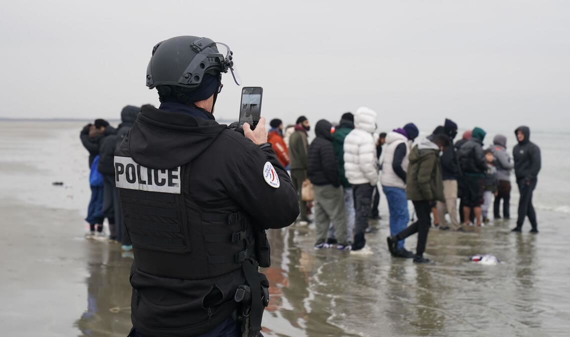 Ein Mitglied der französischen Behörden filmt eine Gruppe von Menschen, bei denen es sich vermutlich um Migranten handelt, die am Strand von Gravelines, Frankreich, warten, während sie versuchen, ein kleines Boot zu besteigen, um den Ärmelkanal zu überqueren.