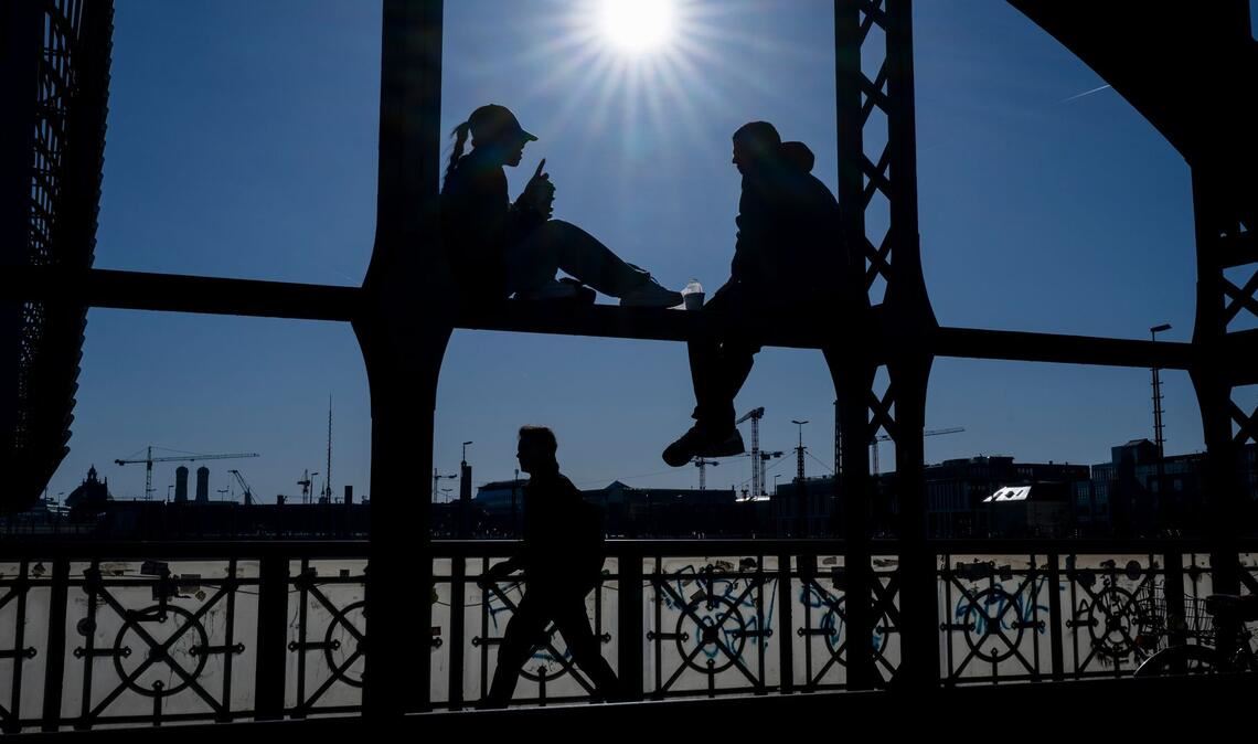Ein Pärchen sitzt in der Sonne auf dem Geländer der Hackerbrücke in München.