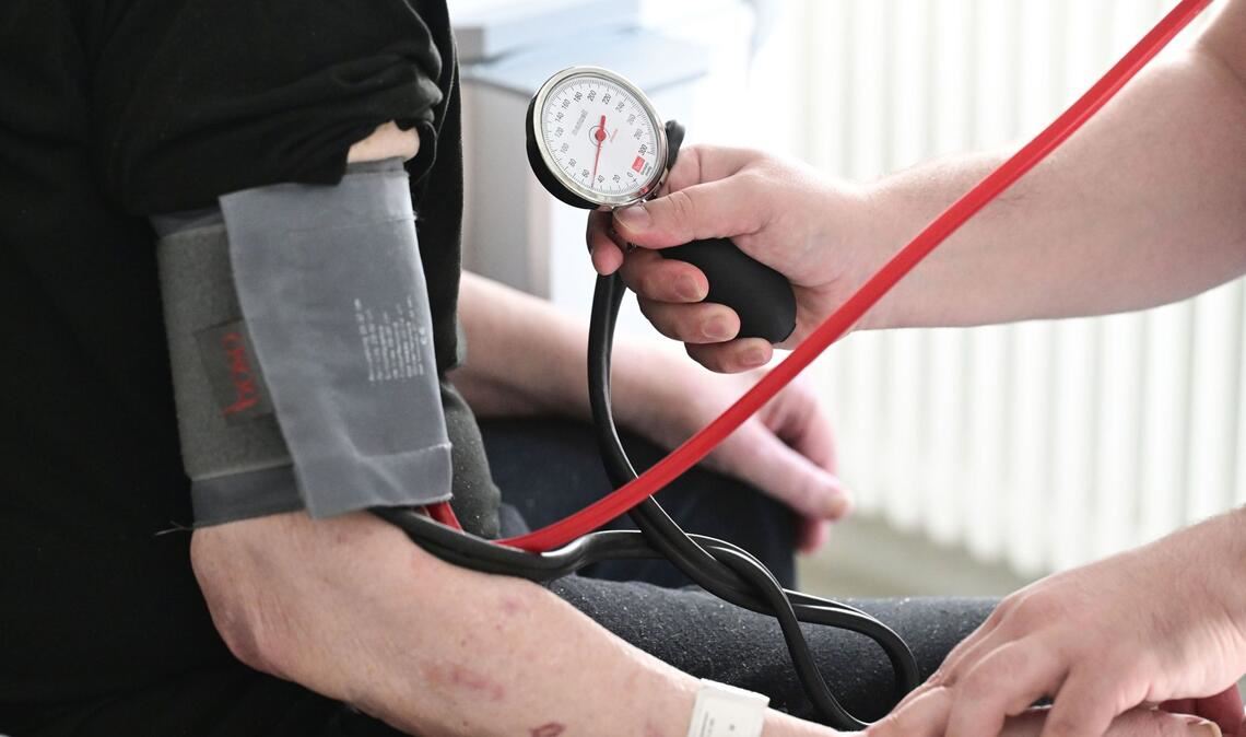 Ein Pfleger misst in einem Krankenhaus auf einer Station bei einem Patienten den Blutdruck.