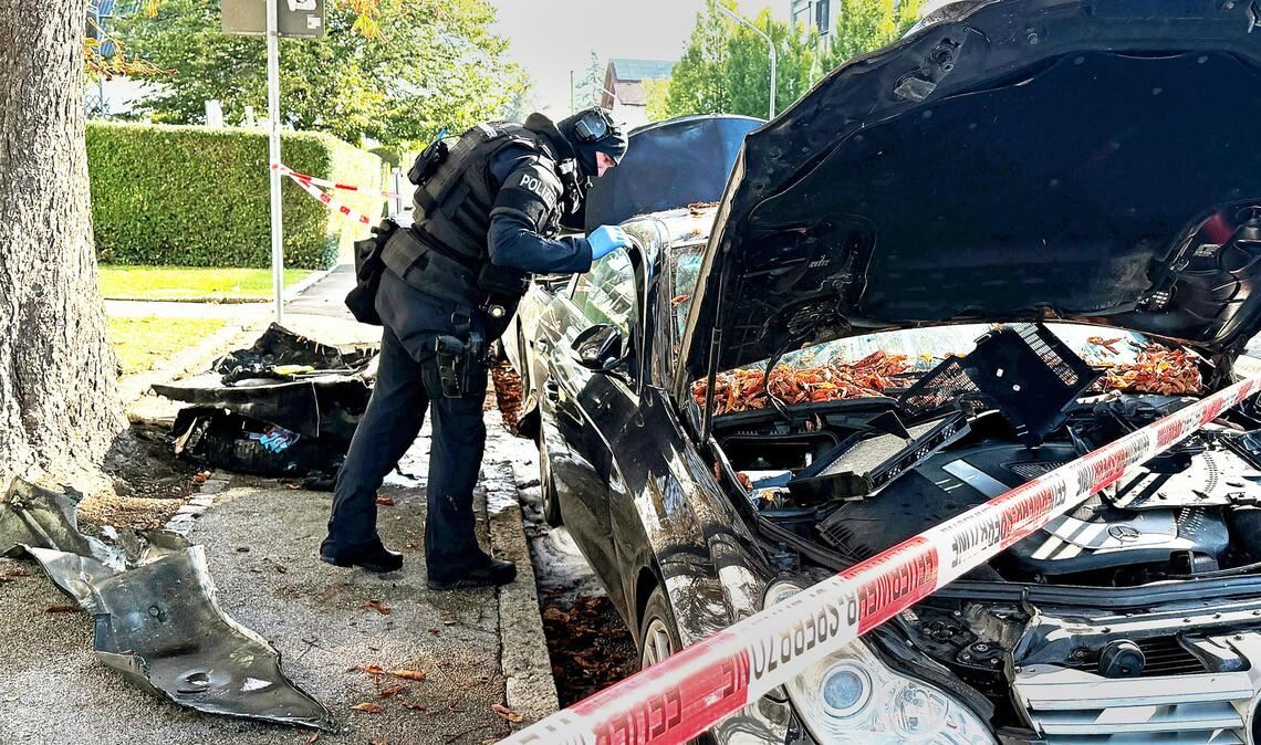 Ein Polizist mit Schutzweste steht an einem PKW, der gebrant hatte. Ein Brand in einem Münchner Einfamilienhaus hat einen Großeinsatz von Polizei und Feuerwehr ausgelöst.