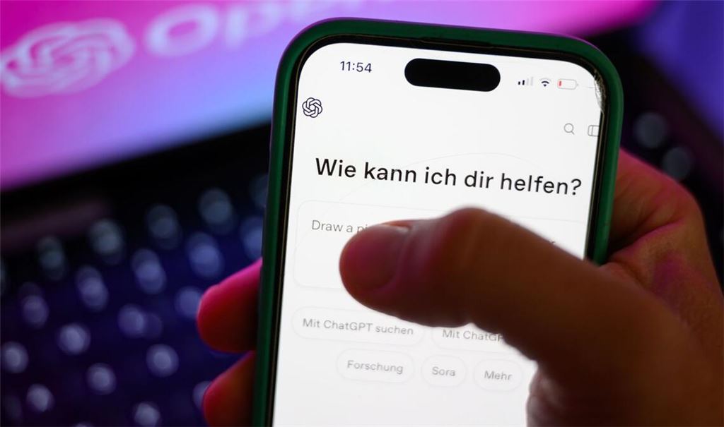Ein Smartphone mit dem KI-Chatbot ChatGPT ist vor dem Logo des US-Softwareunternehmens OpenAI zu sehen. Das KI-Unternehmen hat eine Kindersicherung angekündigt (Symbolfoto).