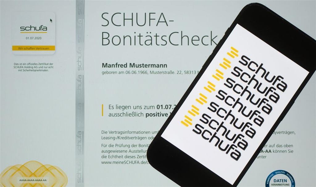Ein Smartphone mit dem Logo der Wirtschaftsauskunftei Schufa liegt auf einem Display mit einem Musterdokument eines Schufa-Bonitätszertifikat.