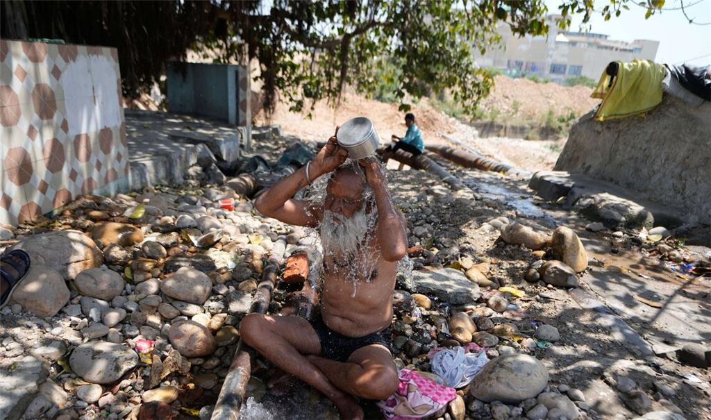 Ein heiliger Mann kühlt sich an einem heißen Tag in der indischen Stadt Jammu mit Wasser ab.