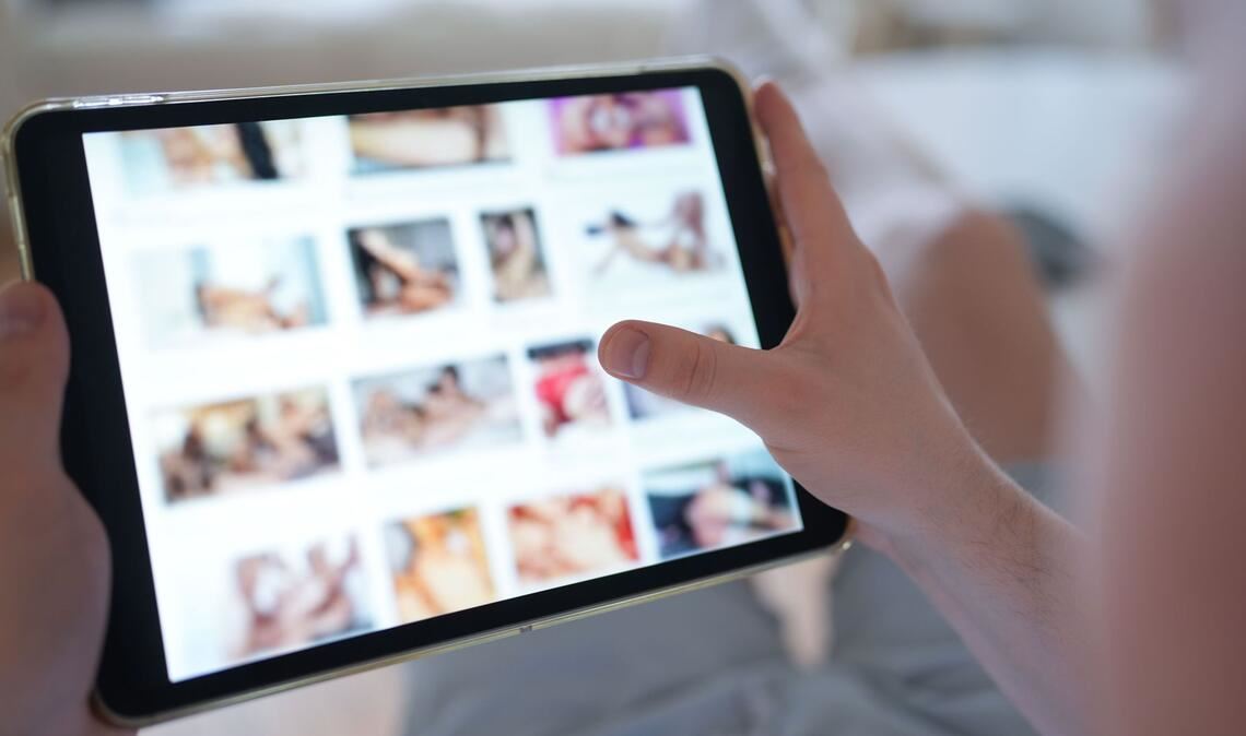 Ein junger Mann schaut sich auf einem Smartphone eine Porno-Internetseite an (gestellte Szene).