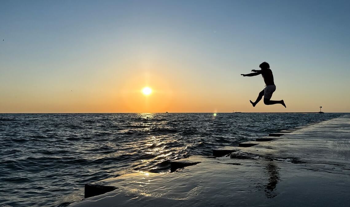 Ein junger Mann springt am frühen Morgen in Chicago von der Promenade am „Oak Street Beach“ in den Lake Michigan.