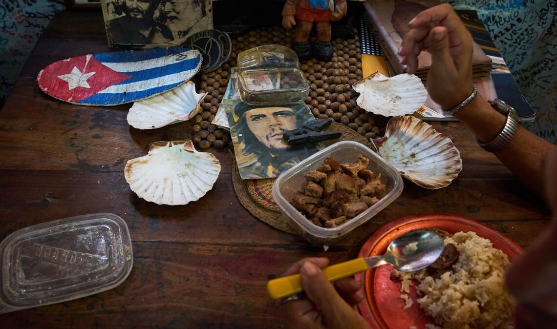 Eine Angestellte eines Souvenirgeschäfts in Havanna isst neben Bildern von Che Guevara, Fidel Castro und Ernest Hemingway.