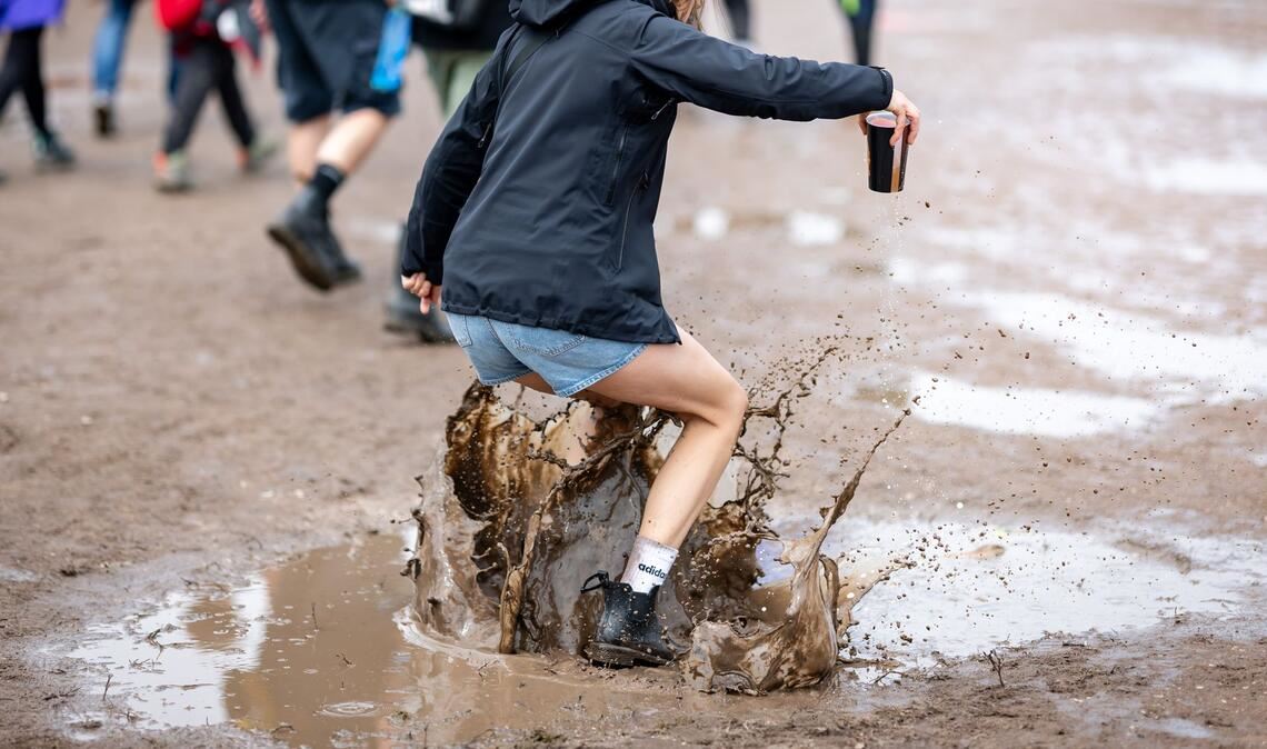 Eine Besucherin des Open-Air-Festivals "Rock im Park" springt in eine Pfütze.