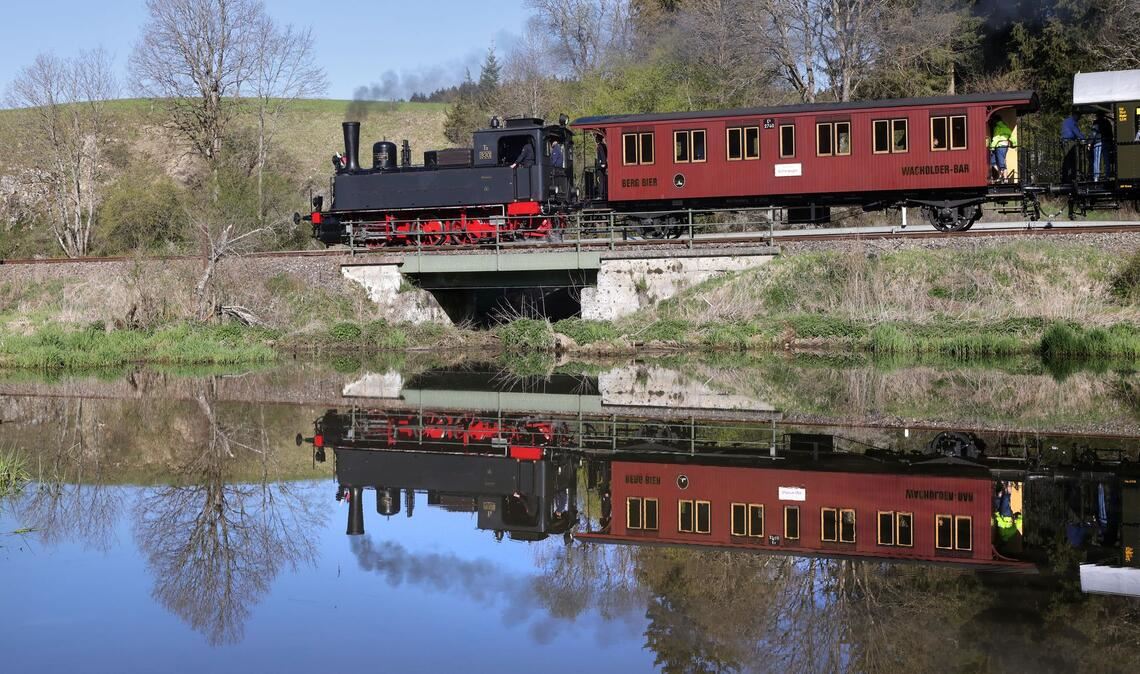 Eine Dampflokomotive ist auf der Schwäbischen Alb unterwegs und spiegelt sich in einem Gewässer.