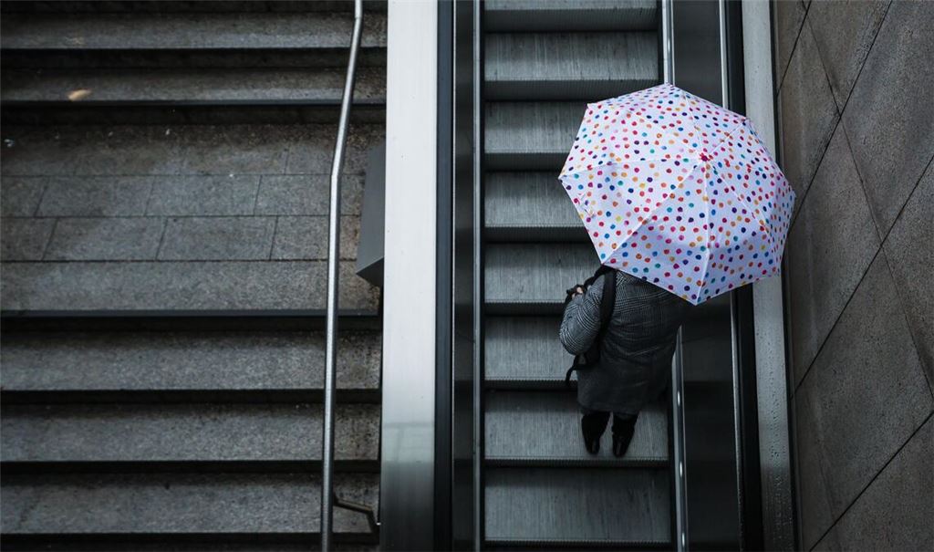 Eine Frau fährt mit ihrem Regenschirm eine Rolltreppe hinauf. Das Wetter soll in der Region Stuttgart in den nächsten Tagen wechselhaft bleiben.