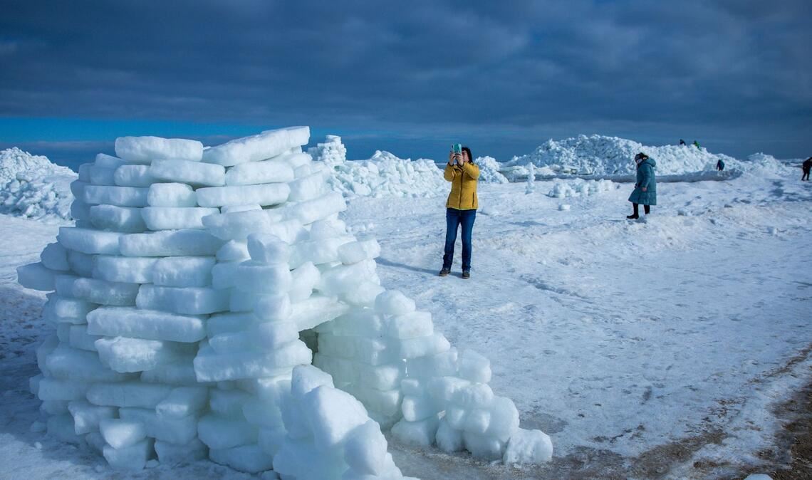 Eine Frau fotografiert ein aus Eisstücken gebautes Iglu vor meterhohen Eisbergen am Ostseestrand auf der Insel Usedom.