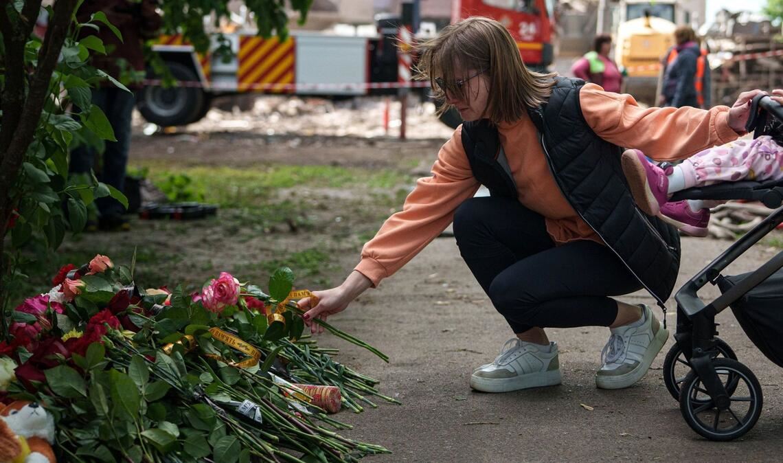 Eine Frau legt Blumen vor einem Haus ab, das nach einem russischen Angriff schwer beschädigt wurde. Nach Angaben von „Save the Children“ sind bislang mehr als 3.500 Kinder  in der Ukraine gestorben. (Archivfoto).
