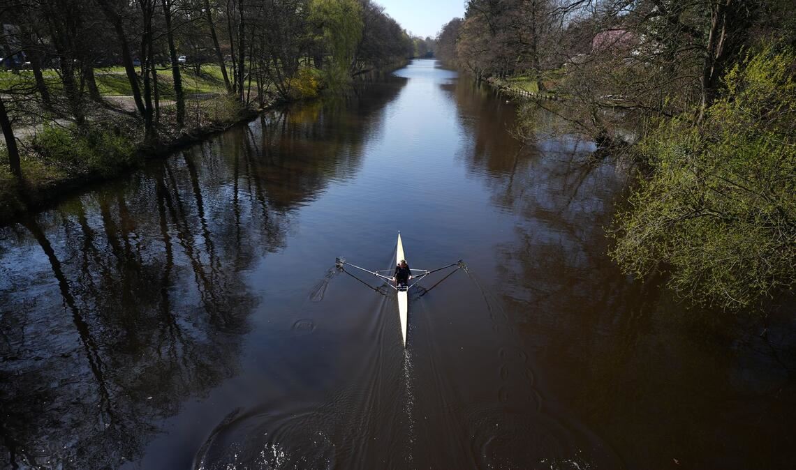Eine Frau rudert mit ihrem Kajak bei schönstem Sonnenschein auf der Alster in Richtung Außenalster.