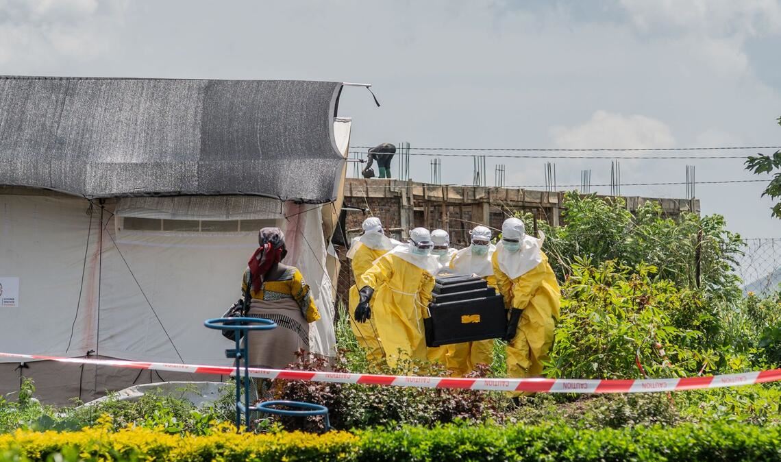 Eine Frau verfolgt, wie Mitarbeiter des Roten Kreuzes in Schutzanzügen den Sarg eines an Ebola Verstorbenen aus einem Gesundheitszentrum in Rwampara, Kongo, tragen.