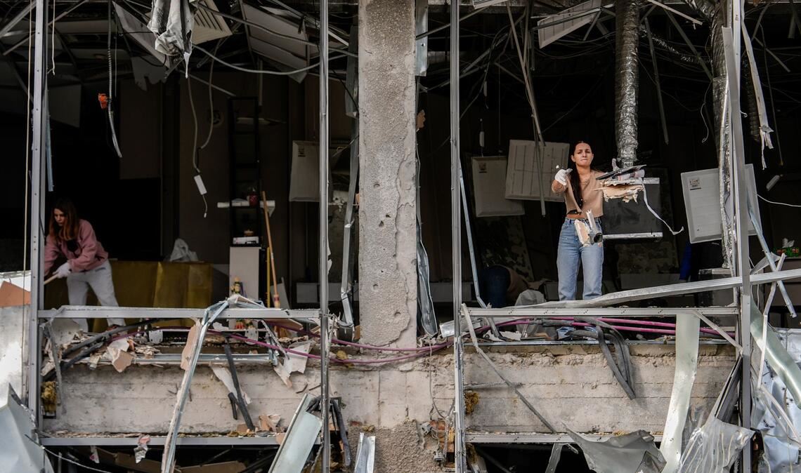 Eine Frau wirft Schutt nach draußen, während sie einen  Friseursalon in Kiew aufräumt, der bei einem russischen Angriff beschädigt wurde.