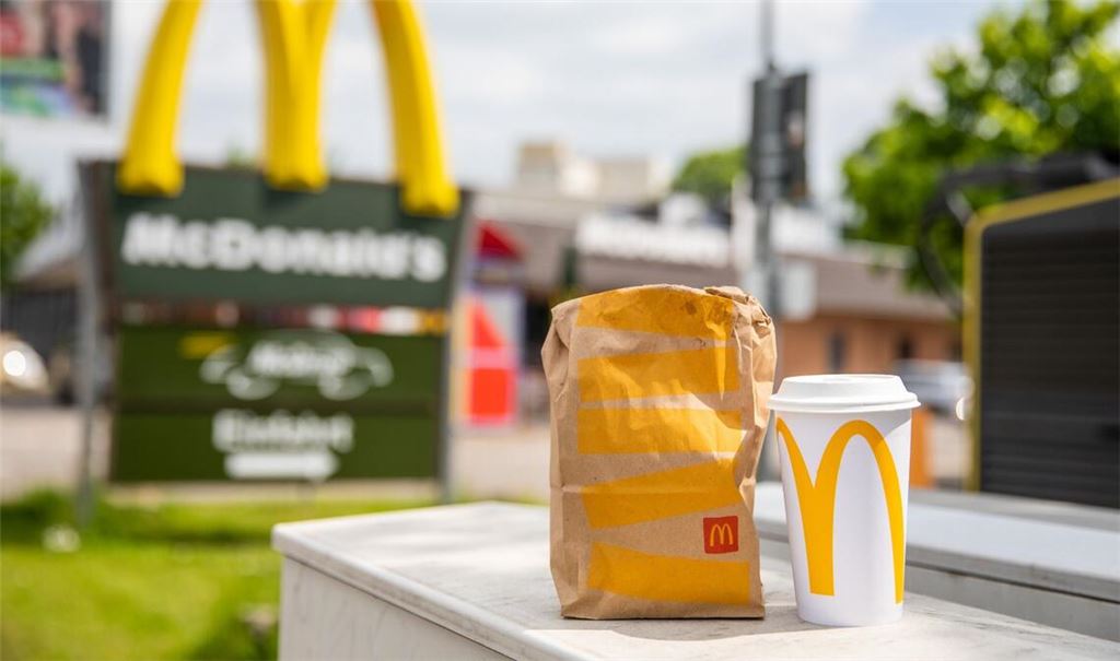 Eine McDonald's To-go-Tüte und ein dazugehöriger To-go-Becher stehen vor einer Tübinger McDonald's Filiale.