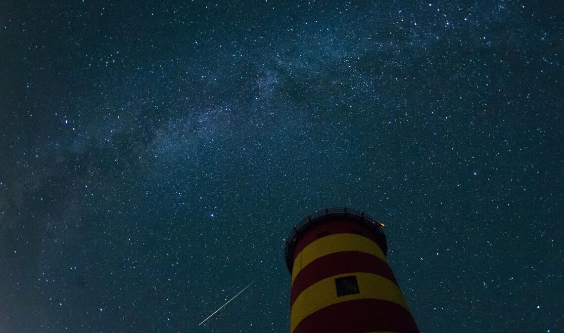 Eine Sternschnuppe leuchtet im August 2015 über dem Pilsumer Leuchtturm in Niedersachsen am Nachthimmel.