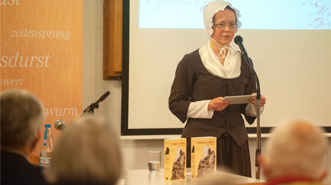 Eine Zeitreise ins Dürrmenz des 18. Jahrhunderts unternehmen die fast 80 Zuhörer im Gemeindehaus gemeinsam mit Autorin Carolin Becker – und das nicht nur durch ihr Romandebüt „Sieben Leben – Brunnengasse“, sondern auch durch passende Kleidung.Fotos: Fotomoment/Deeg