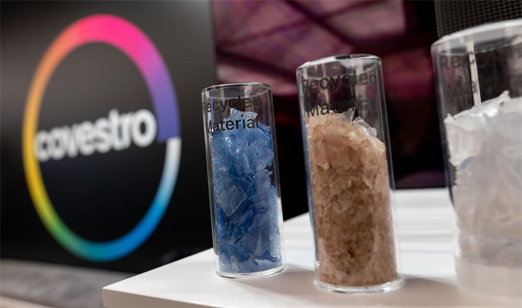 Eine deutsche Firma wird arabisch: Das Logo des Spezialchemie-Konzerns in einem Firmen-Showroom, davor Gläser mit Covestro-Materialien.