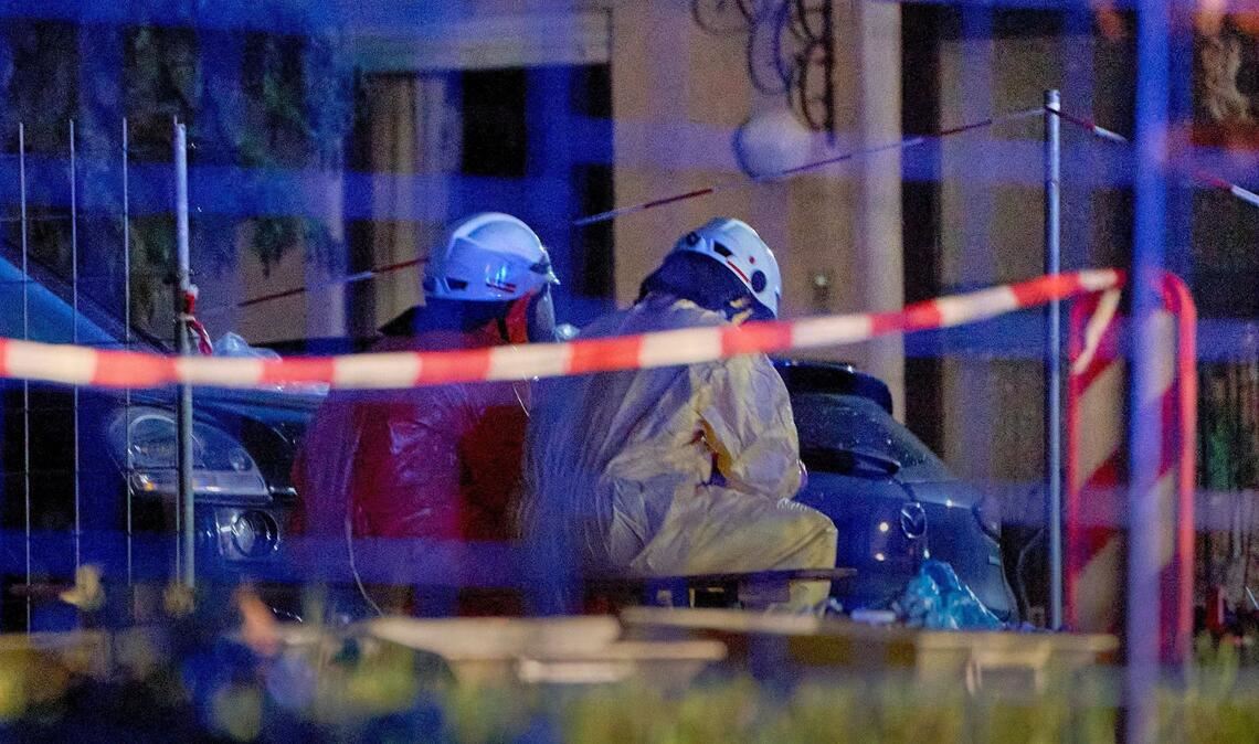 Einsatztkräfte in Schutzanzügen und mit Gasmasken sitzen im hessichen Runkel hinter einer Absperrung.