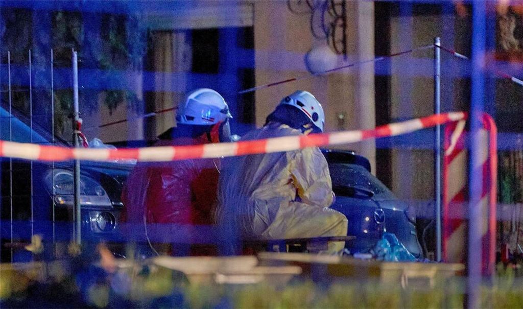 Einsatztkräfte in Schutzanzügen und mit Gasmasken sitzen im hessichen Runkel hinter einer Absperrung.