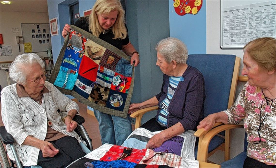 Elke May (2.v.li.) zeigt drei Bewohnerinnen der Demenzstation eine Nestel-Decke.