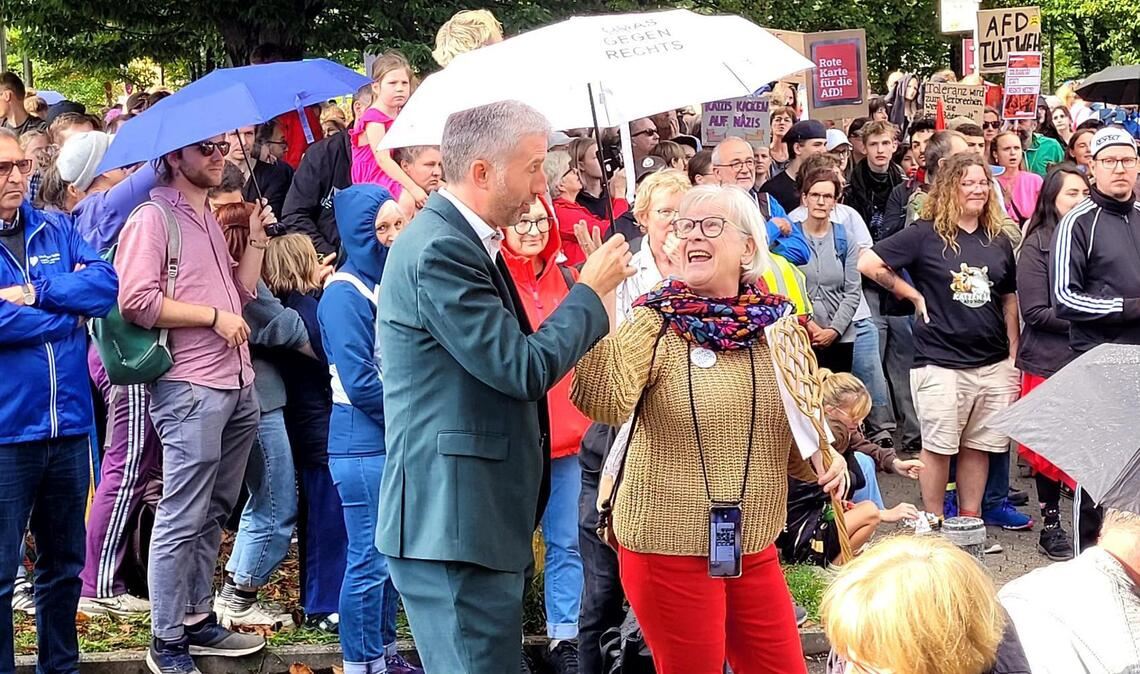 Es regnet kurzzeitig. Eine Frau reicht Palmer einen Schirm.