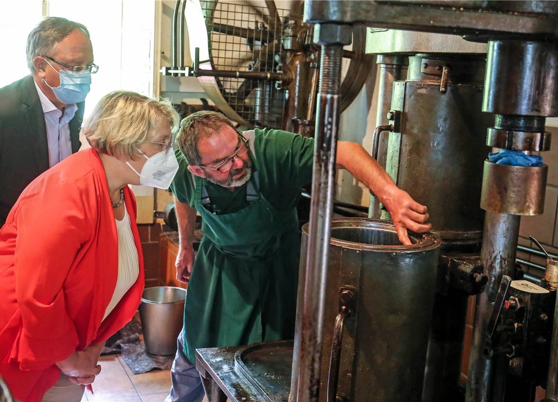 Von der Ölmühle bis zur Familienherberge Fast 120 Jahre alt: Karl-Heinz Arnold (re.) zeigt Katja Mast und Andreas Stoch die Finessen der historischen Ölmühle, die noch so geschmiert läuft wie am ersten Tag. Foto: Goertz