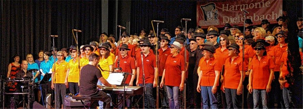 Finale beim Jubiläumskonzert von Martin Falk (li.): Alle Sänger präsentieren gemeinsam auf einer übervollen Bühne die Ballade von Udo Lindenberg „Hinterm Horizont geht’s weiter“.