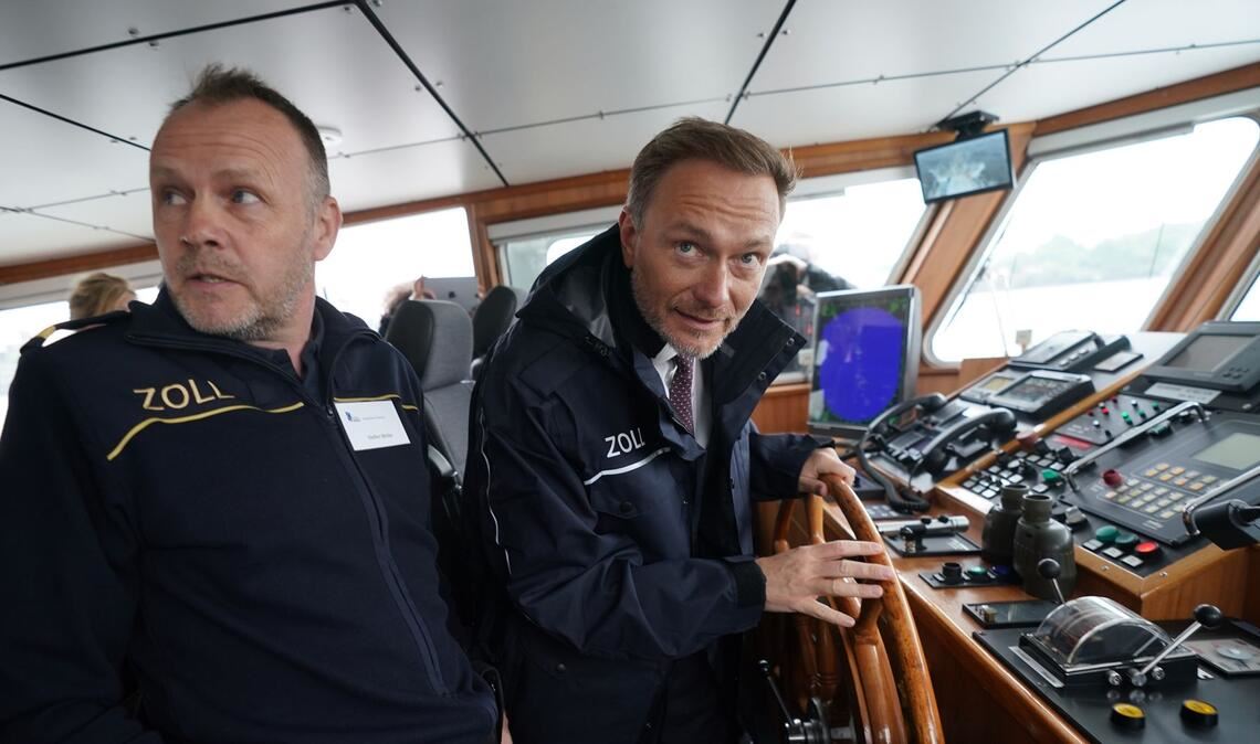 Finanzminister Christian Lindner (r)  steuert das Zollboot "Kehrwieder", links Zollkapitän Steffen Molter.
