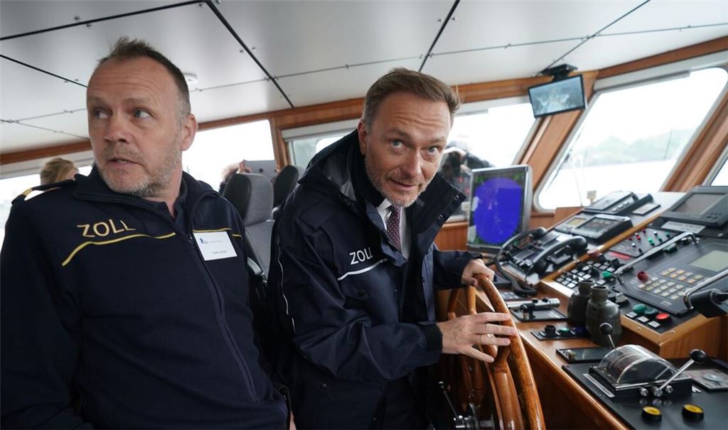 Finanzminister Christian Lindner (r)  steuert das Zollboot "Kehrwieder", links Zollkapitän Steffen Molter.