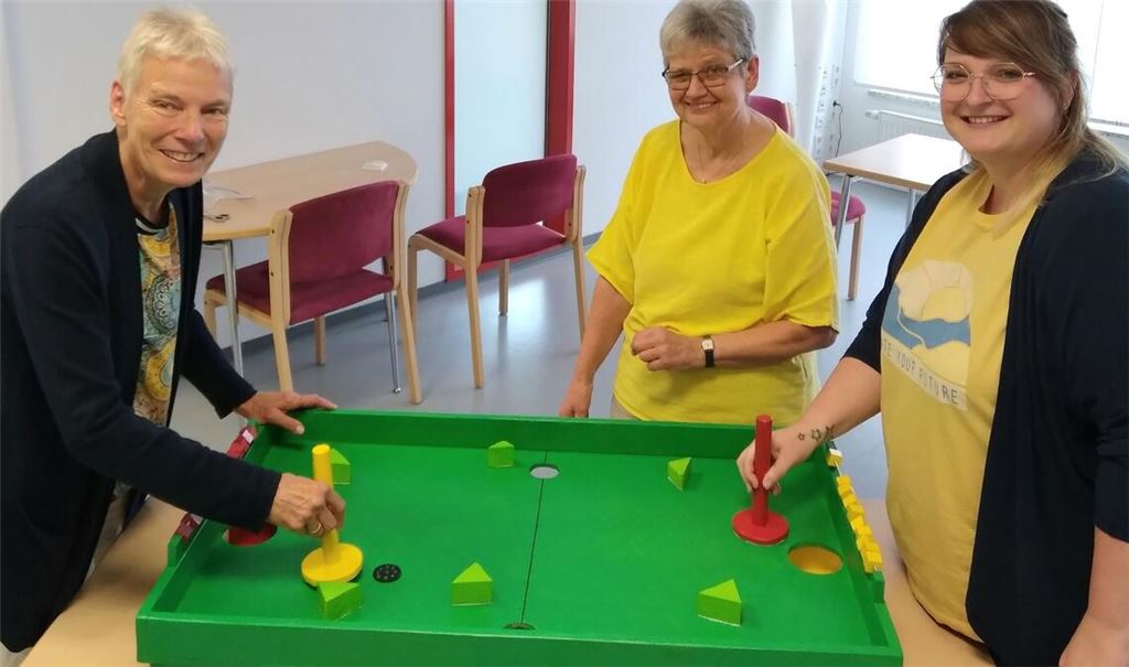 Freuen sich über das neue Flitzpuck-Spiel, das die Handwerker-Männergruppe des Consilios gebaut hat: Barbara Straub von der Gesamtkirchengemeinde Mühlacker (li.) und ihre Kollegin Susanne Striegel (re.). In der Mitte die betreuende Ergotherapeutin Ina Hornung. Foto: Consilio/Karin Watzal