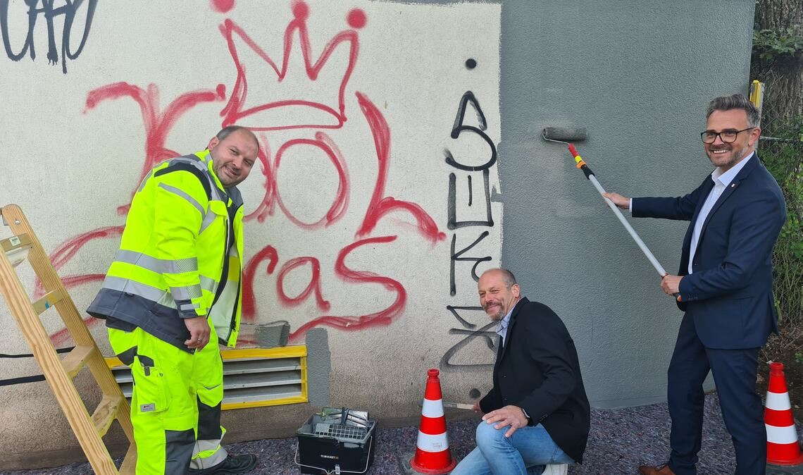 Für das Pressebild unterstützen Oberbürgermeister Peter Boch (v.re.) und Jens Hartmann, Abteilungsleiter Betrieb bei den Technischen Diensten, Malermeister Tobias Hermann beim Überstreichen. Foto: Metzbaur