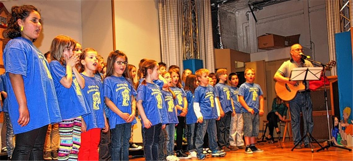 Geburtstagsfeier zum 20-jährigen Bestehen: Schüler der Kirsten-Boie-Grundschule singen „Unsere Schule hat einen coolen Namen“. Begleitet werden sie dabei von Ex-Schultes Adalbert Bangha mit der Gitarre. 