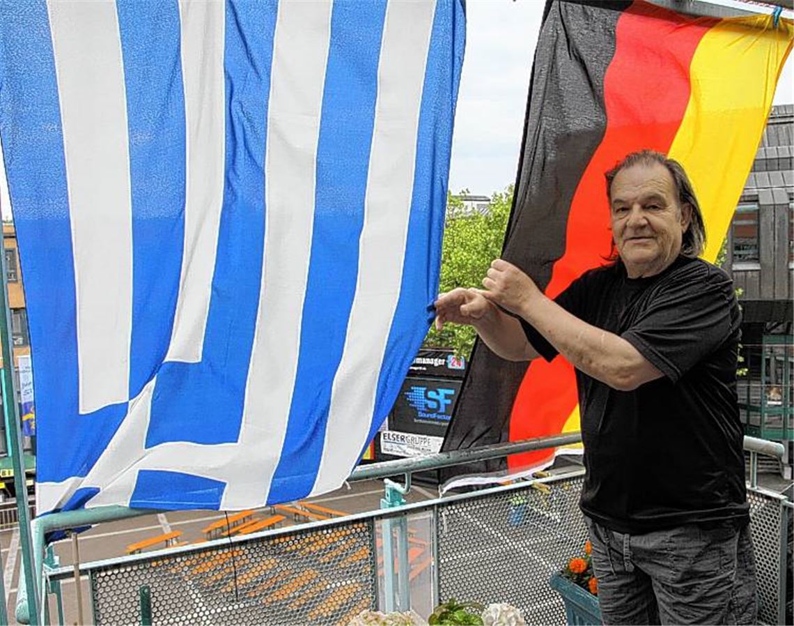 Georgios Kantzos im Zwiespalt der Gefühle. Seinen Logenplatz hoch über dem Kelterplatz hat er seit Wochen deutsch-griechisch dekoriert. Heute Abend nach dem EM-Viertelfinale wird ein Auge lachen, das andere weinen. Foto: Eigner