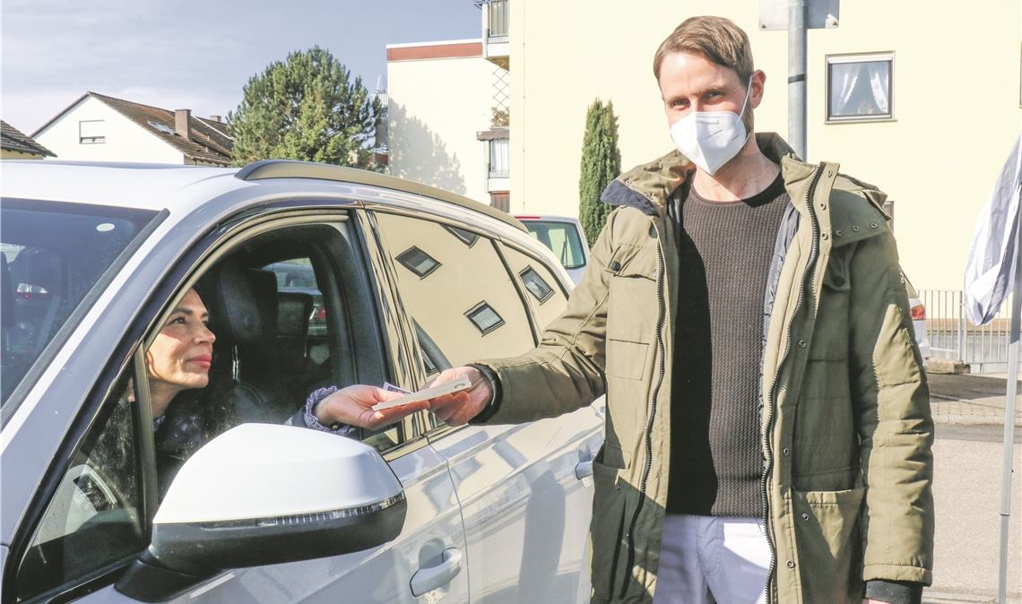 Gero von Langsdorff übergibt in Ötisheim nahe seiner Praxis, wo er Patienten seit vier Wochen an seiner Impfstraße durchs geöffnete Autofenster spritzt, Papiere zur Dokumentation. Wewoda