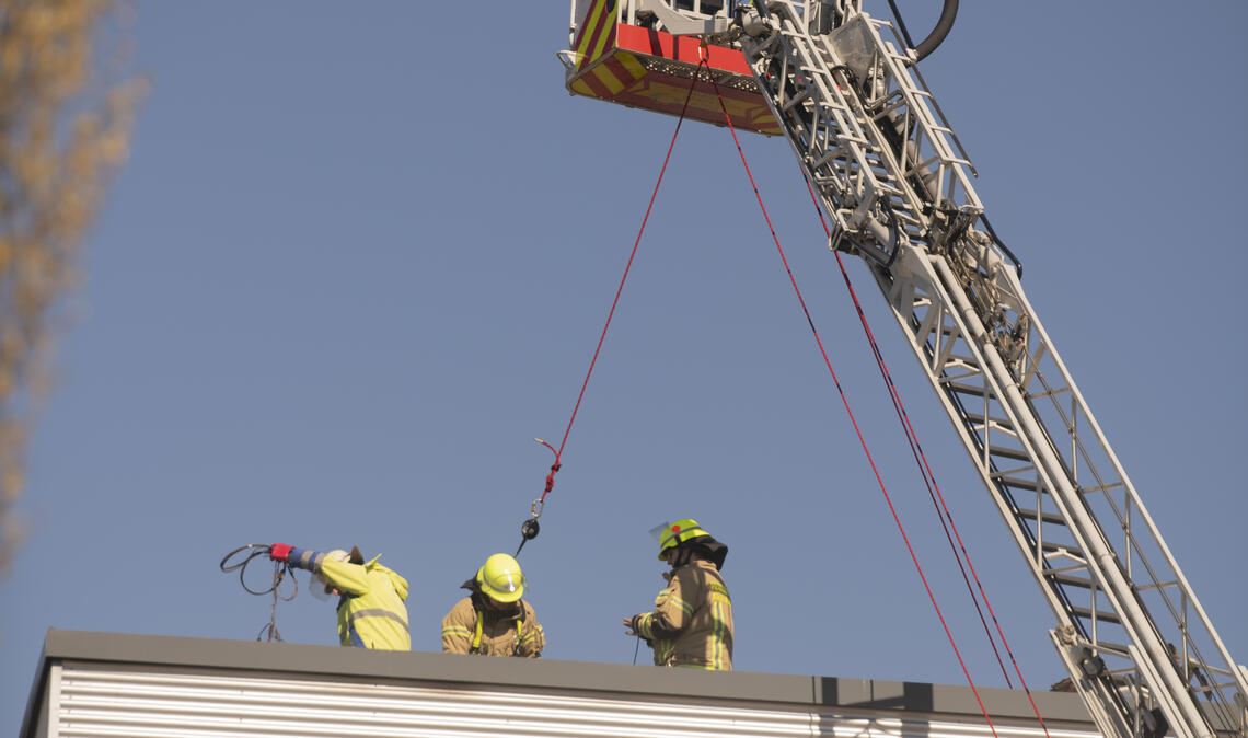 Gesichert vom Korb der Drehleiter aus, arbeiten die Feuerwehrleute auf dem Dach von Elumatec. Foto: Fotomoment