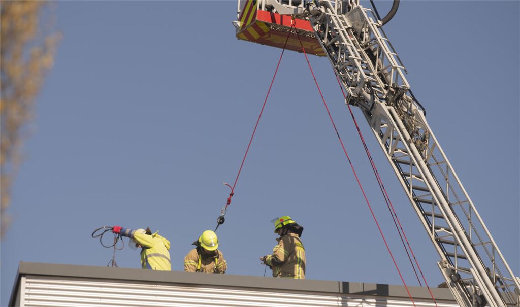 Gesichert vom Korb der Drehleiter aus, arbeiten die Feuerwehrleute auf dem Dach von Elumatec. Foto: Fotomoment