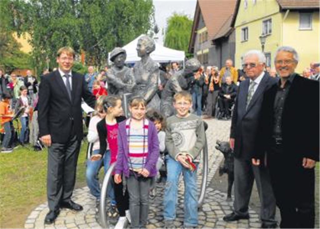 Große Freude über das neue Bertha-Benz-Denkmal, das den Bauschlotter Dorfanger gegenüber der evangelischen Kirche künftig bereichert, herrscht bei der Enthüllung des Kunstwerks. V. li. Bürgermeister Michael Schmidt, Denkmal-Stifter Werner Wild und Künstler Kurt Tassotti mit Kindern der Friedrich-Weinbrenner-Schule, die das Denkmal gleich in Besitz nehmen. Foto: Schott