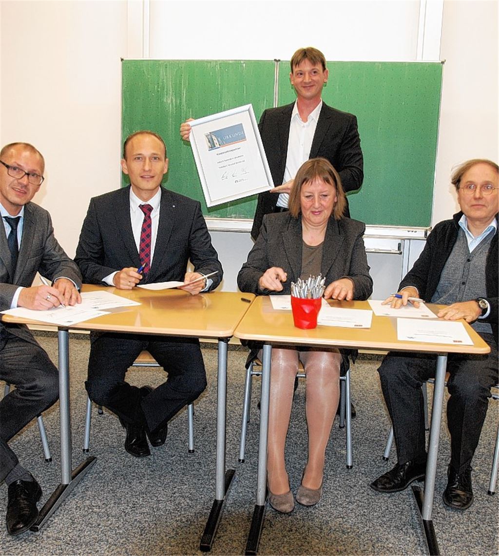 Günter Brecht, Dimitrios Meletoudis, Christine Stamler und Rainer Blank (sitzend von re.) unterzeichnen die Kooperationsvereinbarung. Lehrer Thorsten Dörr zeigt die Urkunde. Foto: Appich