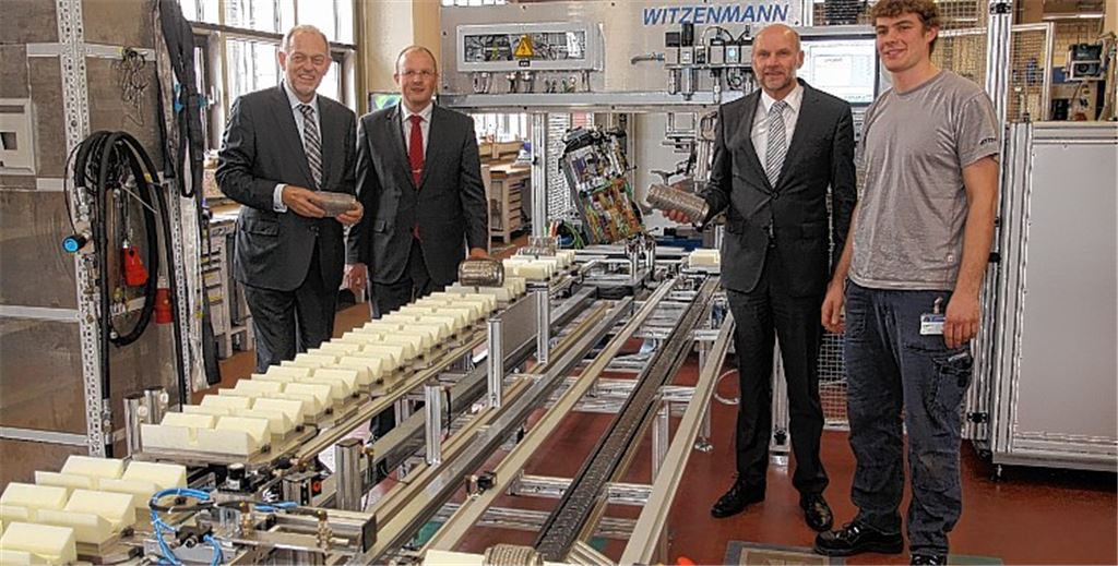 Haben Grund zur Zufriedenheit (v. li.): das Geschäftsführungstrio der Firma Witzenmann Dr. Hans-Eberhard Koch, Dr. Andreas Kämpfe und Dr. Gerhard Flöck mit Mitarbeiter Sascha Rabenseifner neben einem Förderband für den Transport von Entkoppelelementen für Autoabgasanlagen. Foto: Sadler
