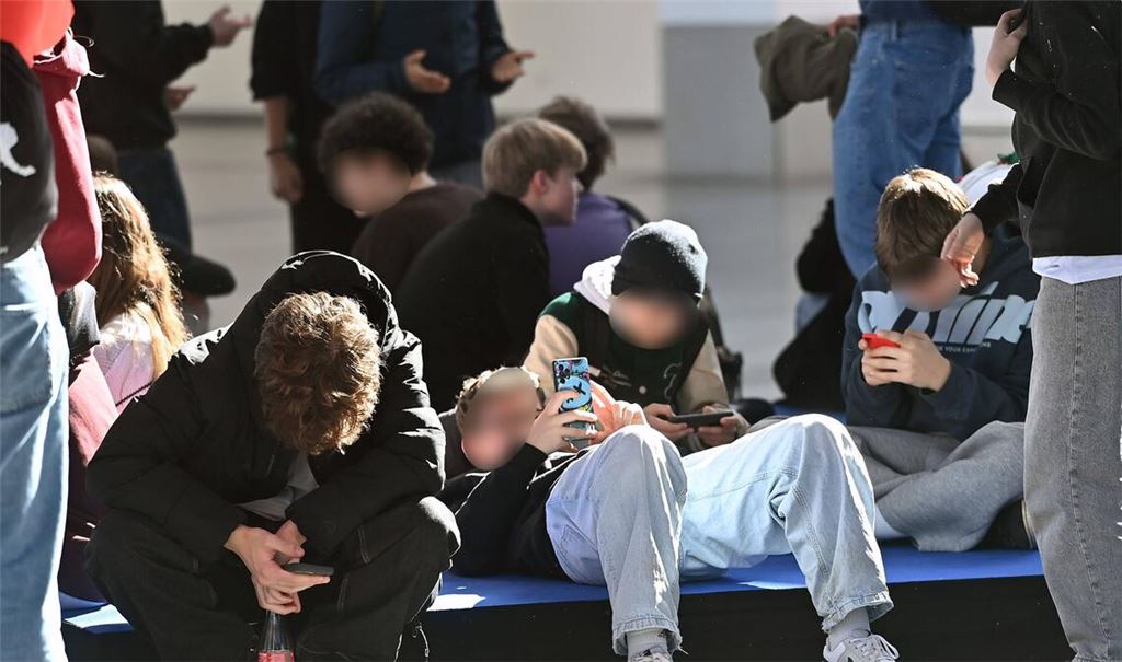 Handy-Sucht: Schüler sitzen während der Pause auf dem Boden und blicken auf ihre Smartphones.