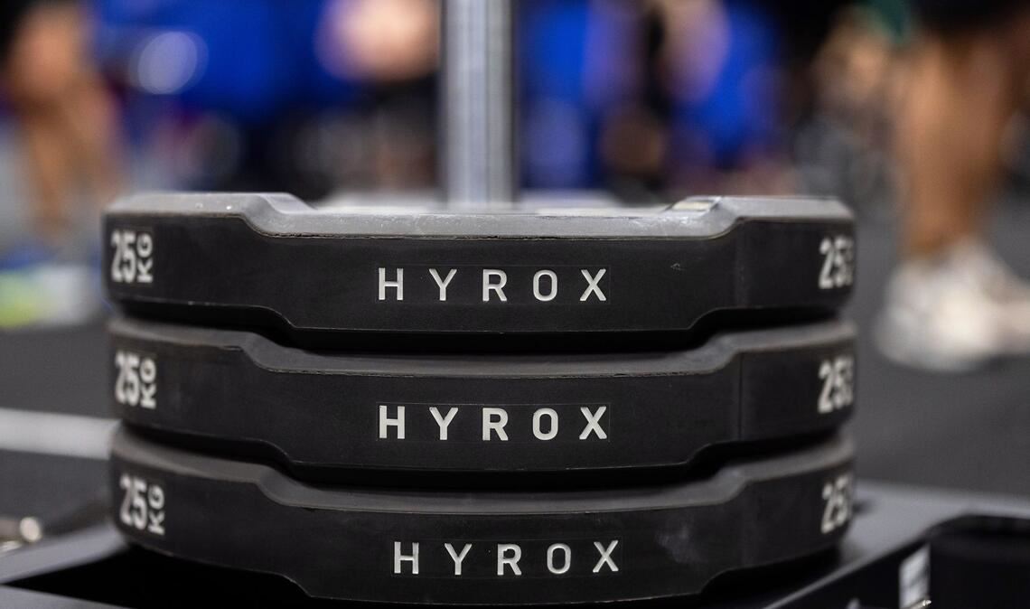 Hantelscheiben mit dem Schriftzug Hyrox an einem Messestand, wo wenig später ein Lauf- und Workout-Wettbewerb stattfinden sollte.