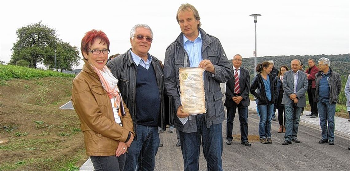 Heinz-Peter Hopp hält die Übergabeurkunde für den neu geschaffenen Milanweg in Händen. Mit ihm freuen sich Ortsvorsteherin Waltraud Piechatzek, Günther Scheible vom Erschließungsträger Scheible BauLand GmbH sowie Bürger, Stadträte und Mitarbeiter der beteiligten Firmen.