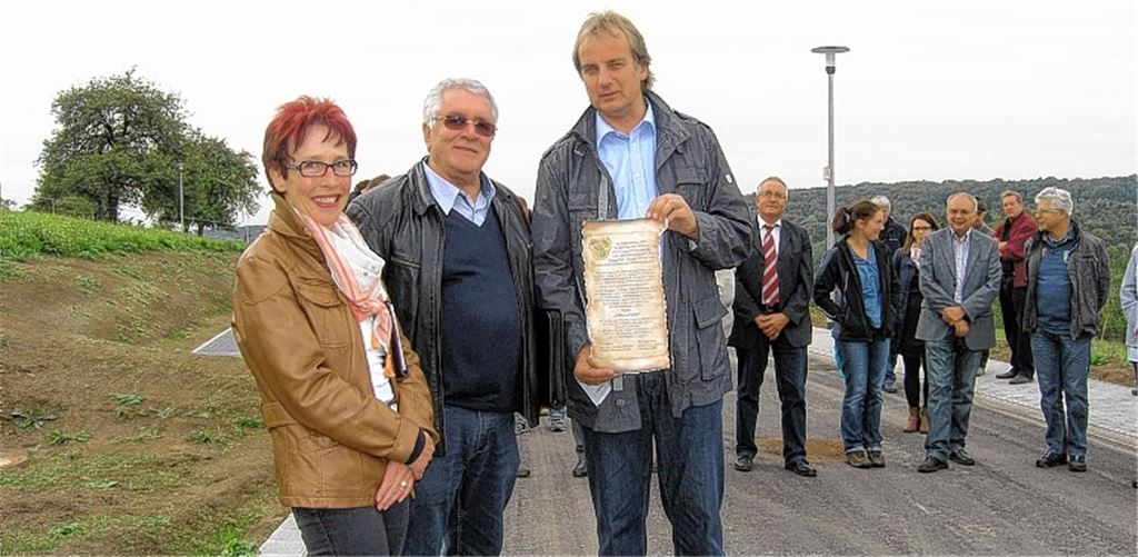 Heinz-Peter Hopp hält die Übergabeurkunde für den neu geschaffenen Milanweg in Händen. Mit ihm freuen sich Ortsvorsteherin Waltraud Piechatzek, Günther Scheible vom Erschließungsträger Scheible BauLand GmbH sowie Bürger, Stadträte und Mitarbeiter der beteiligten Firmen.